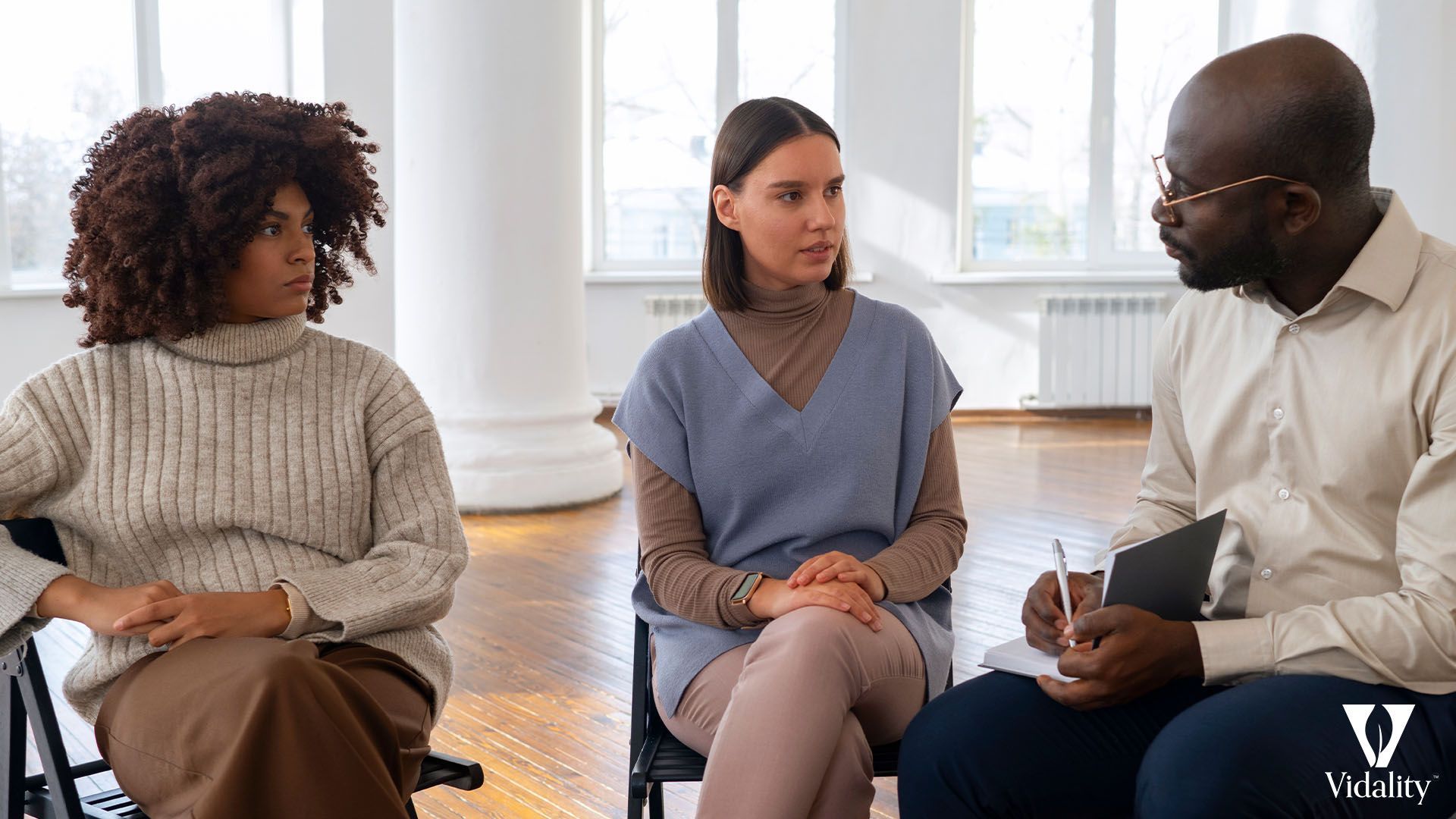 Three individuals engaged in conversation while seated in chairs.