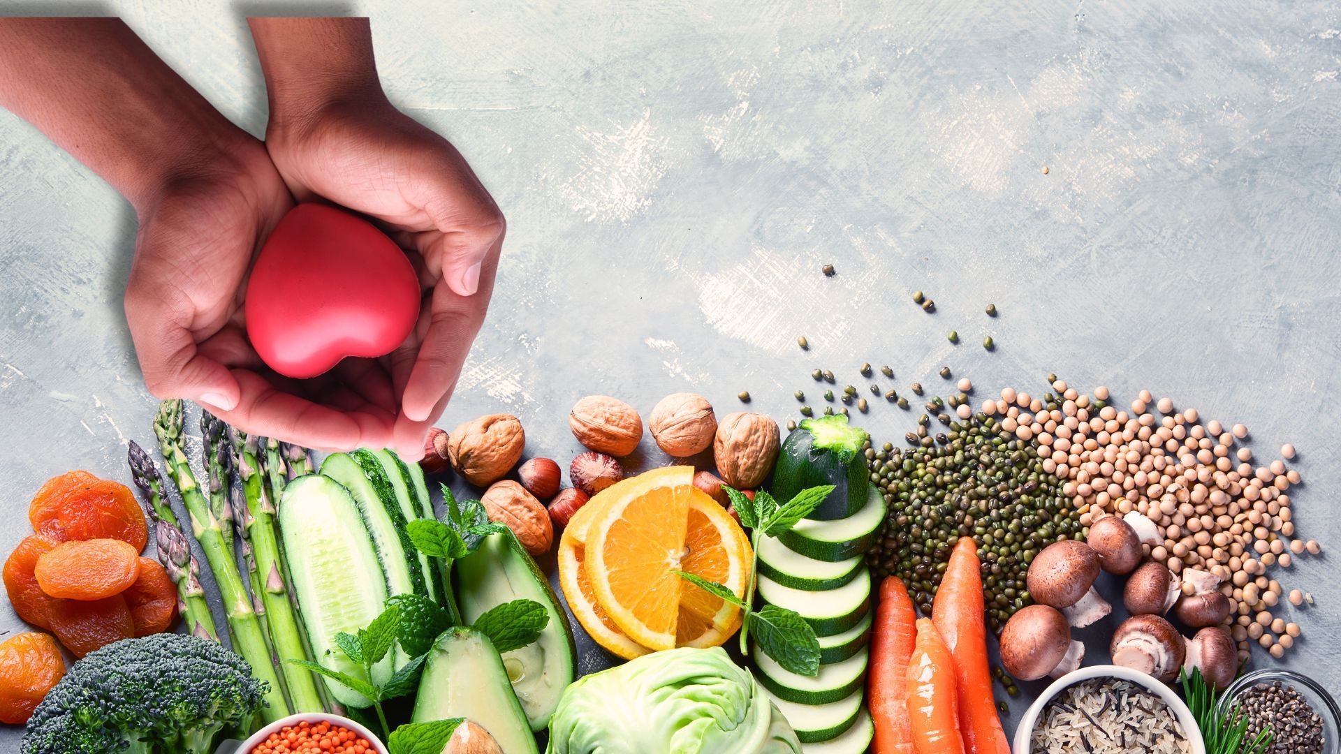 A person holding a red heart amidst a colorful assortment of fruits and vegetables.