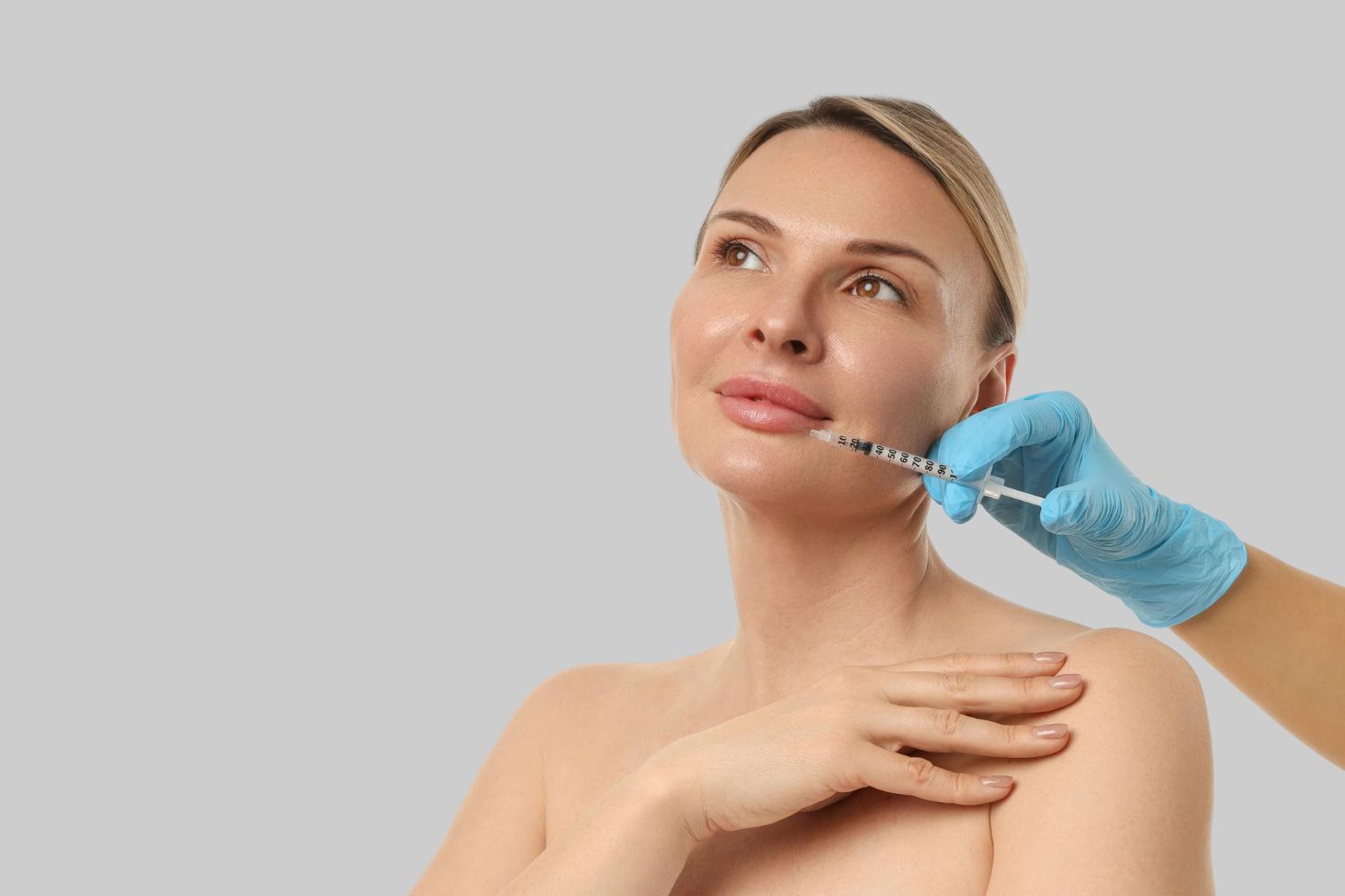 Woman receiving a cosmetic chin injection from a gloved practitioner against a gray background