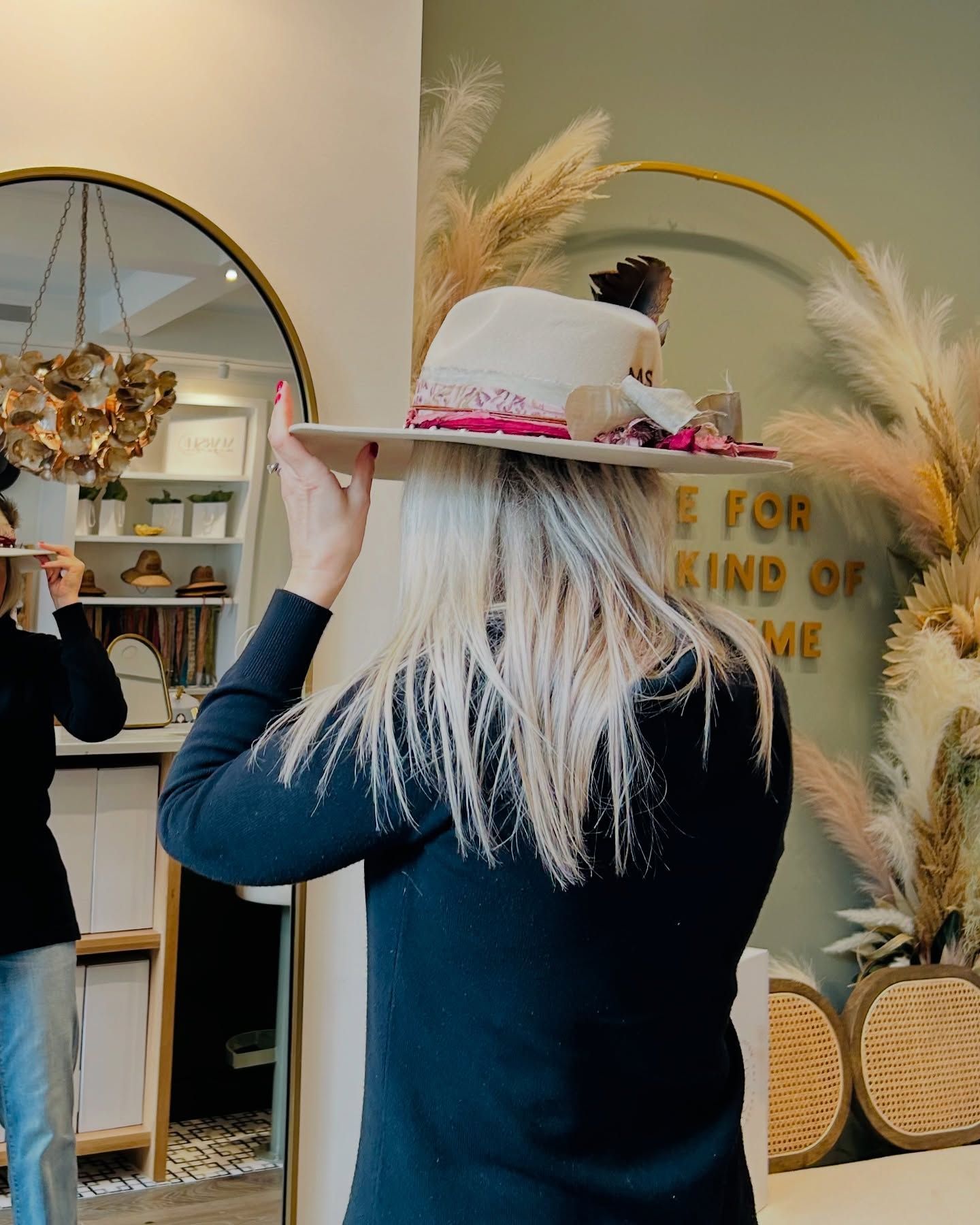 A woman wearing a hat is standing in front of a mirror.