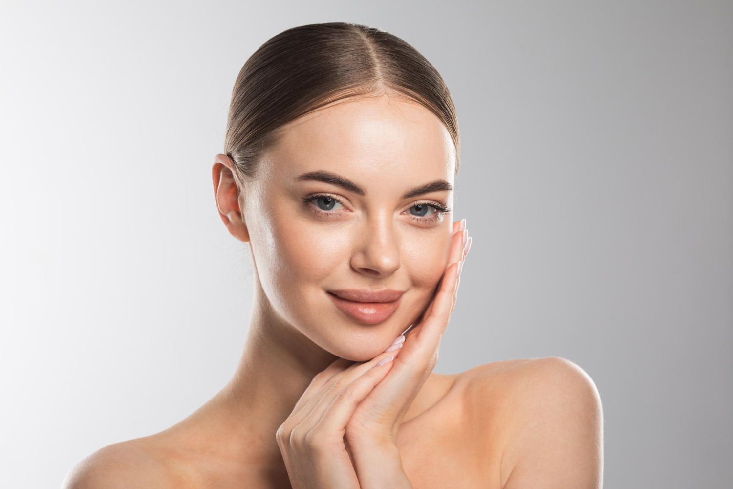 Smiling woman with smooth skin gently touching her face against a light gray background