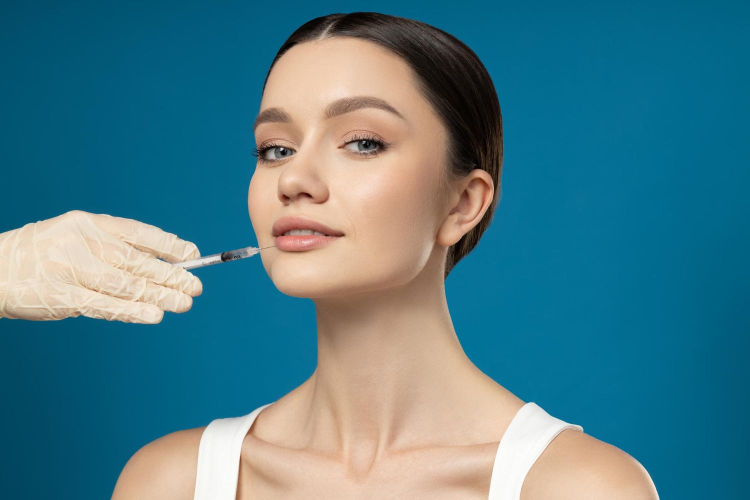 Woman receiving a facial injection from a gloved hand against a blue background