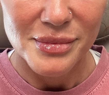 Close-up of a person’s mouth and nose wearing a pink sweatshirt, with a silver nose ring.