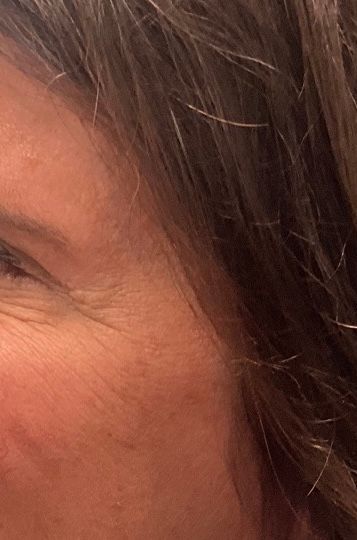 Close-up of a person’s cheek and eye with long brown hair against a warm background