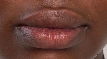 Close-up of closed lips with pink lip gloss on medium-brown skin.