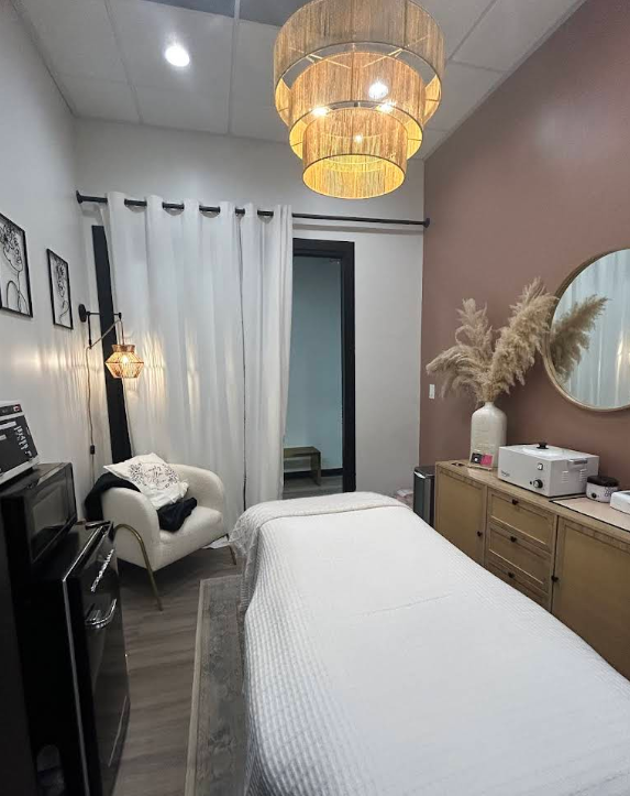 A medspa treatment room with a bed, chair, dresser and mirror.