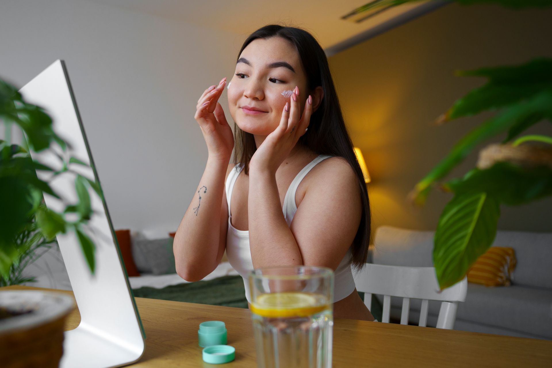 A woman is sitting at a table looking at her face in a mirror.