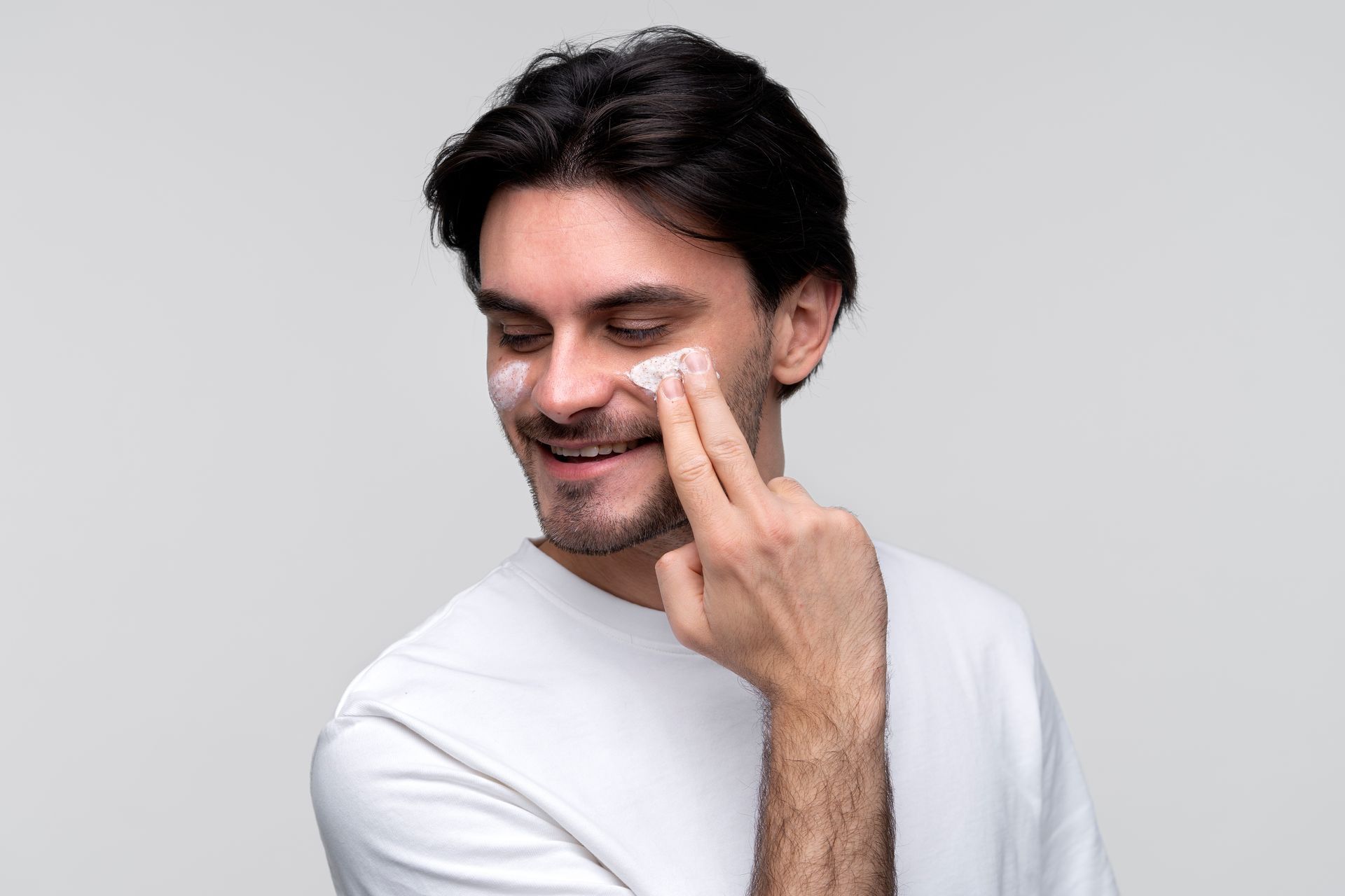 A man is smiling while applying cream to his face.