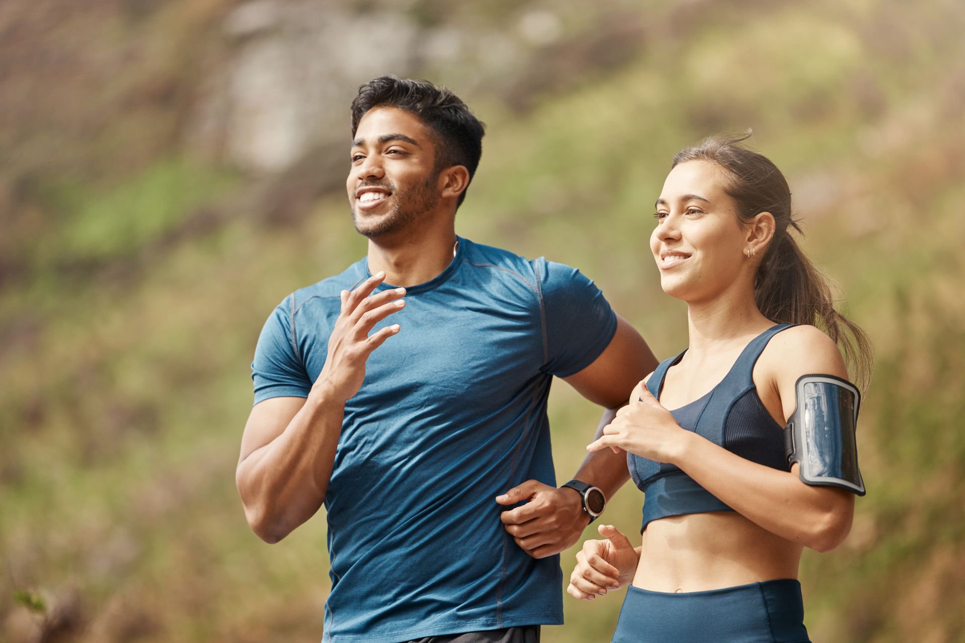 Two runners in athletic wear jogging outdoors, smiling in a wooded area