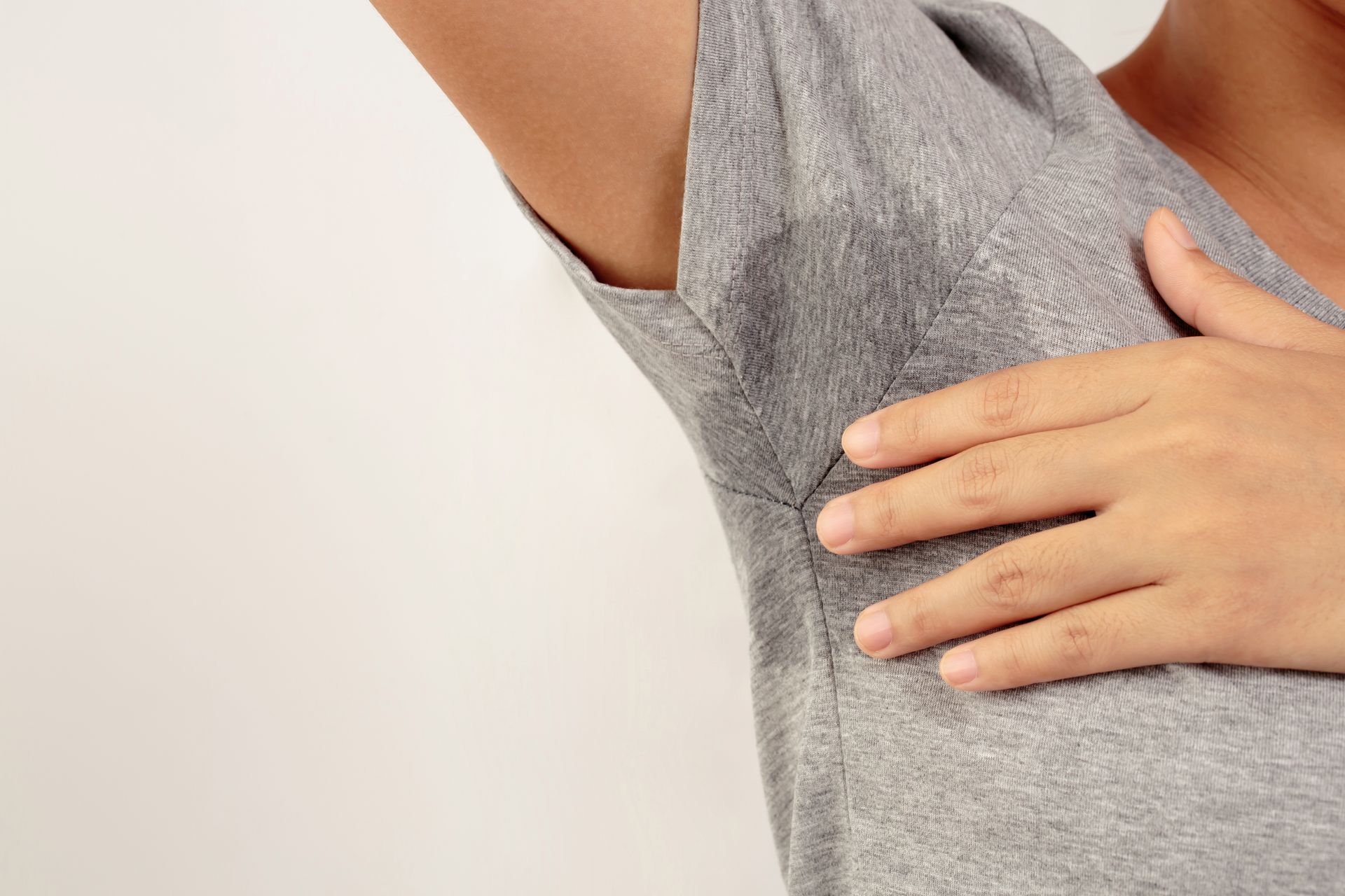 Person holding their armpit in a gray shirt, suggesting underarm discomfort