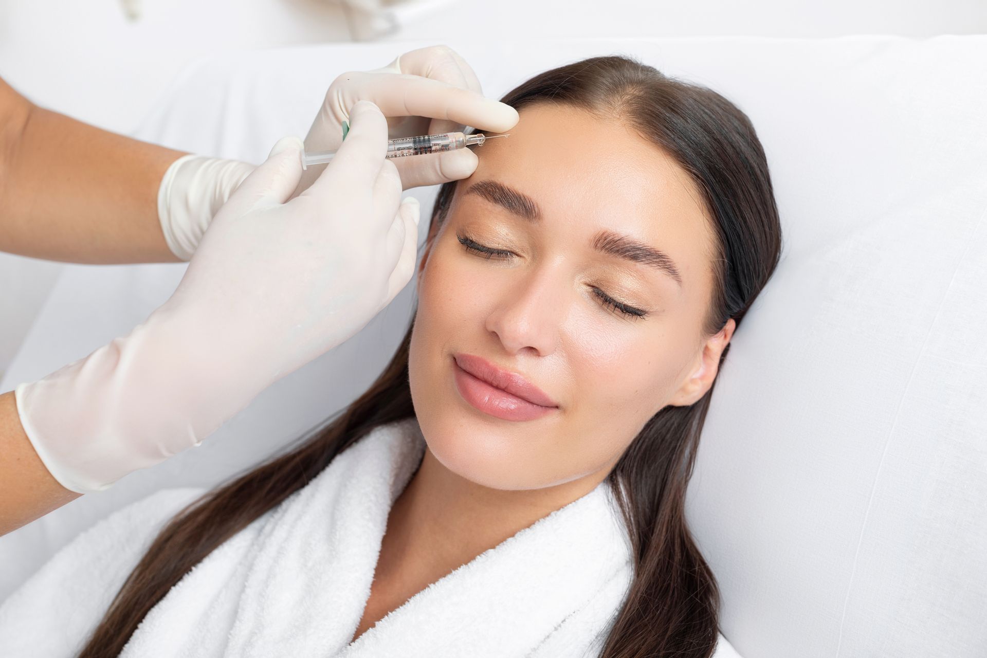 Aesthetic treatment being applied to a woman’s forehead with a handheld device in a spa setting