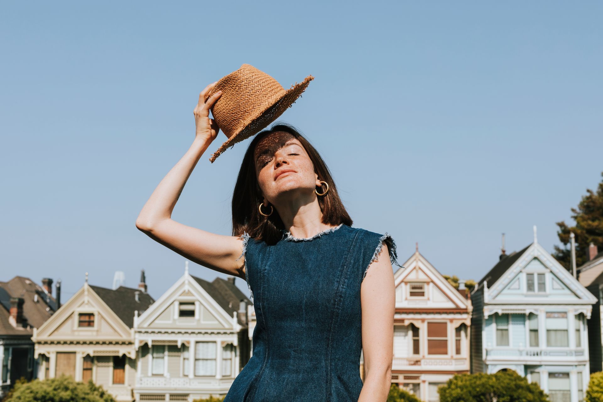 A woman wearing a straw hat is standing in front of a row of houses.