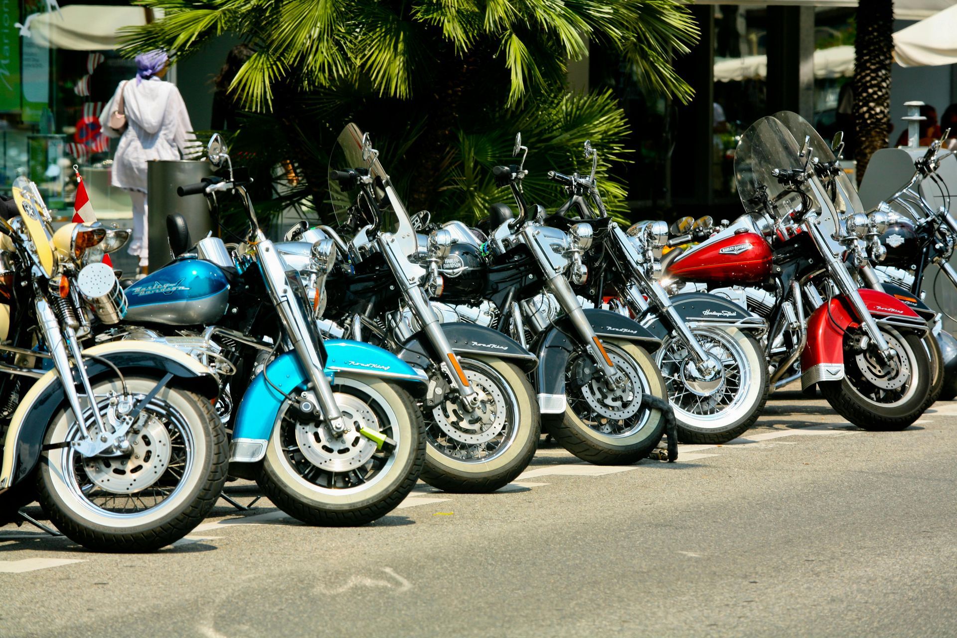 Row of parked vintage motorcycles in blue, cream, silver, and red on a sunny street