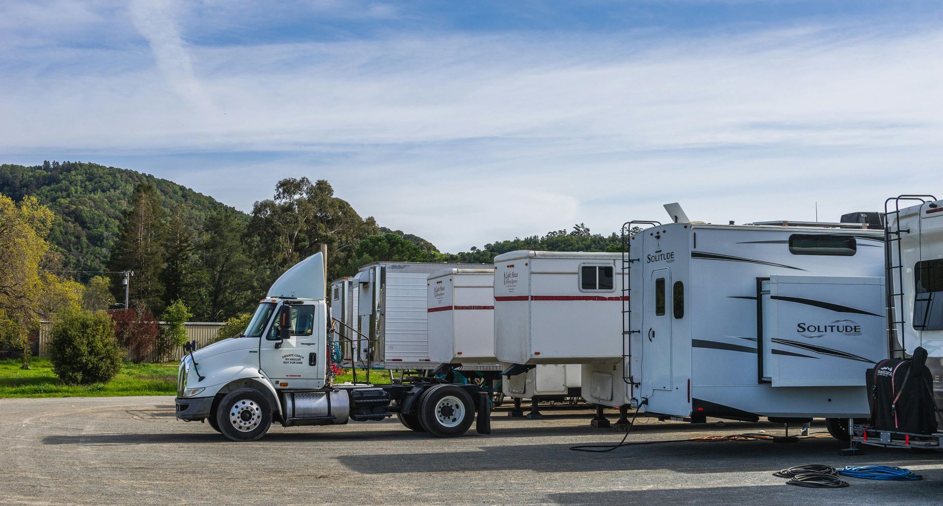 White semi-truck with trailer parked in a lot beside a large RV under a blue sky.