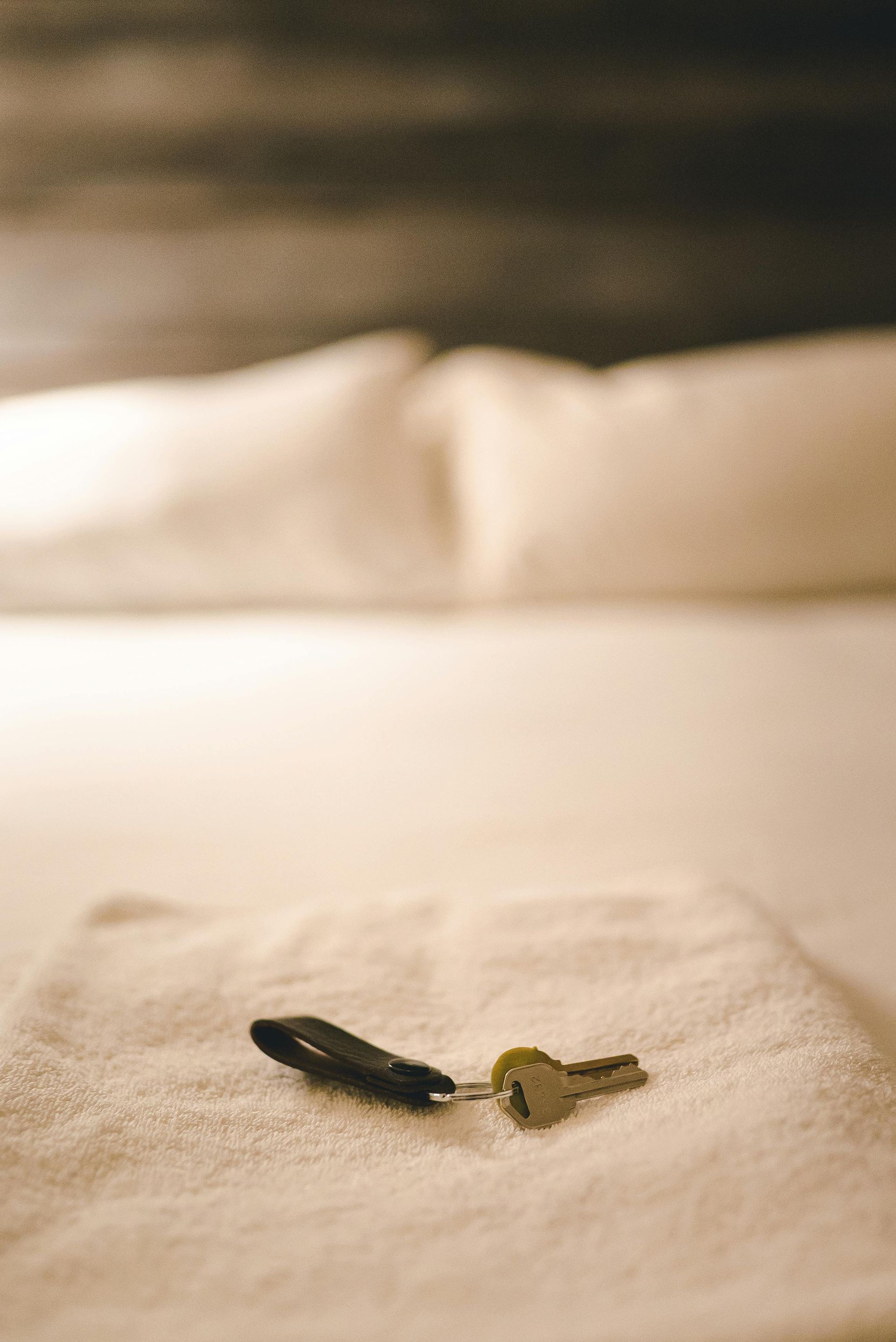 Black and gold key on a white bed, with a blurred pillow in the background