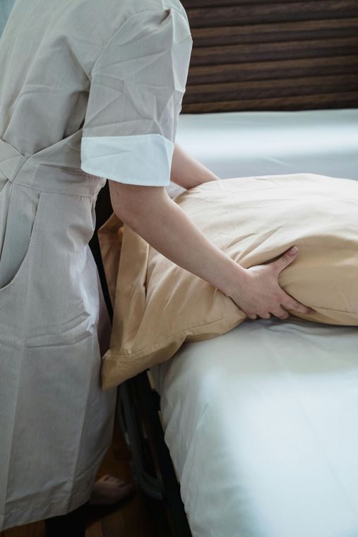Person making a bed, smoothing a beige blanket on a white mattress