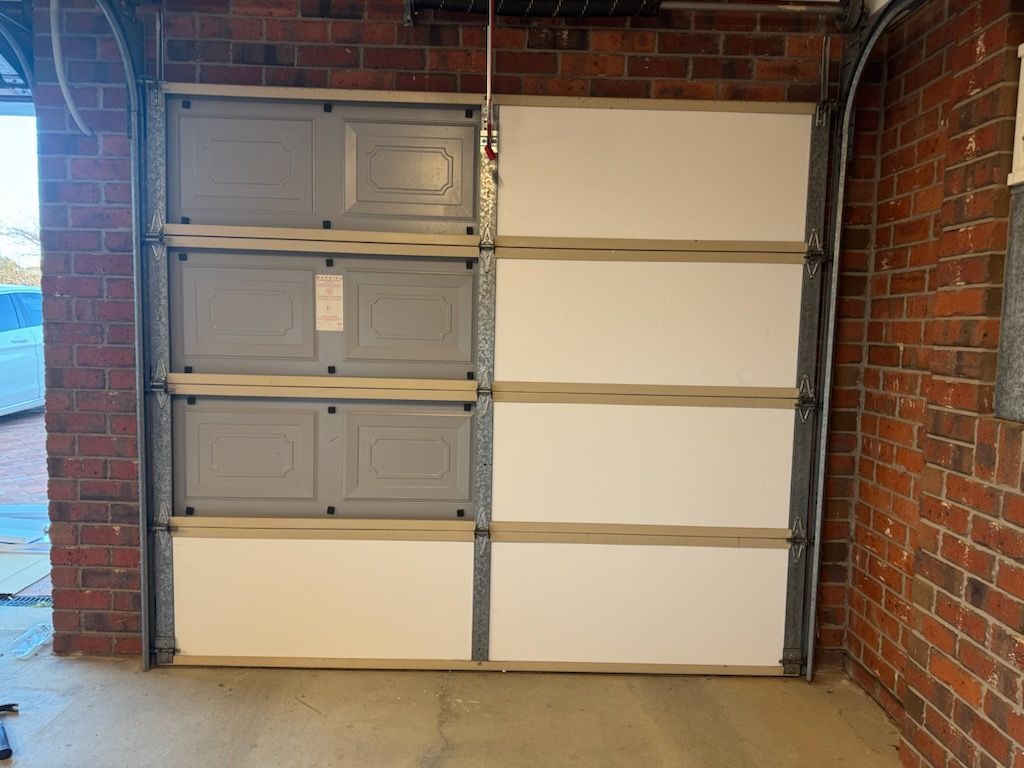 Garage door, partially assembled, with gray and white panels, set in a brick-walled garage.— Vent Wise in Twin Waters, QLD