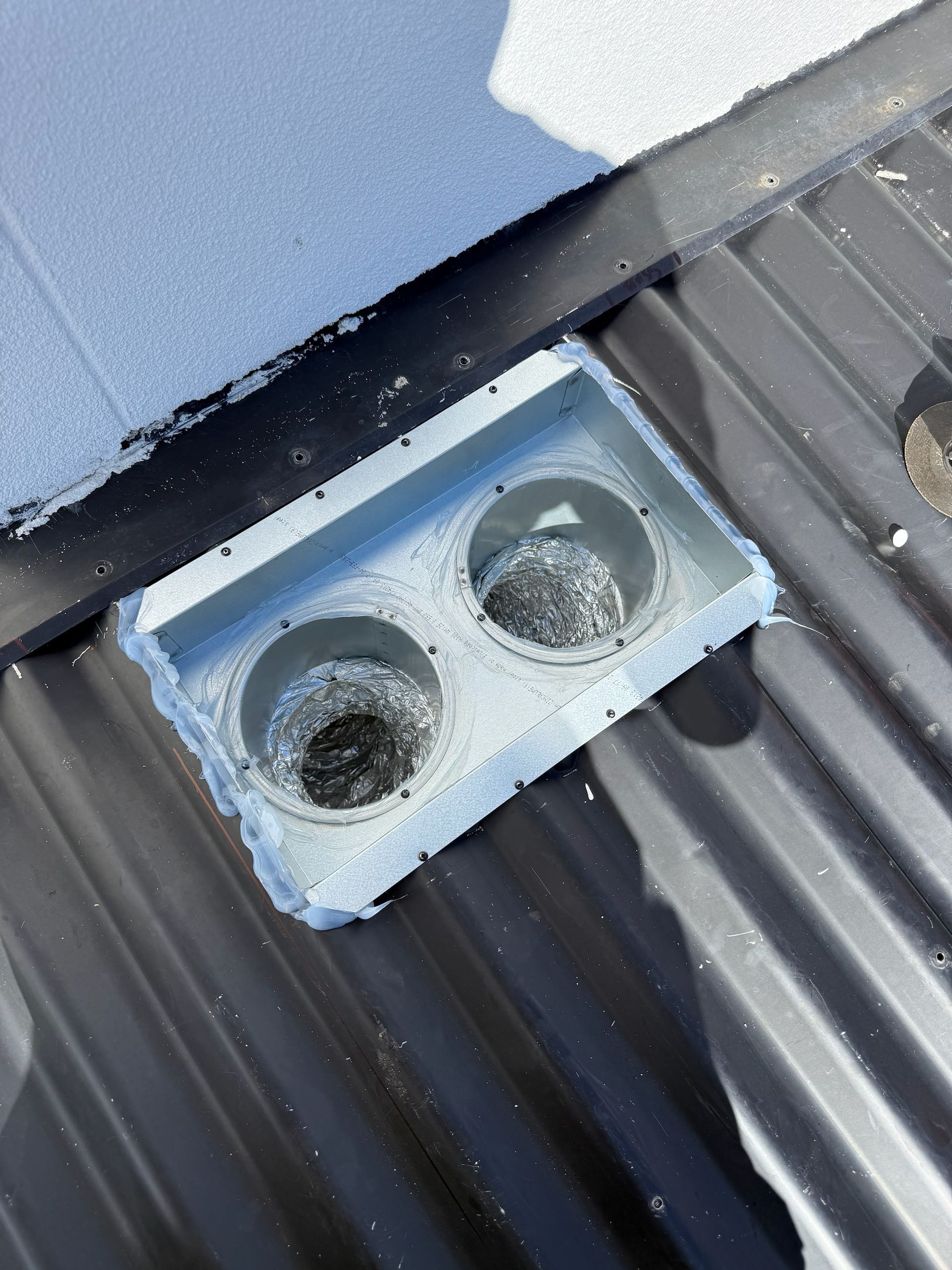 Two vent pipes emerging from a rectangular white housing on a corrugated metal roof.— Vent Wise in Twin Waters, QLD