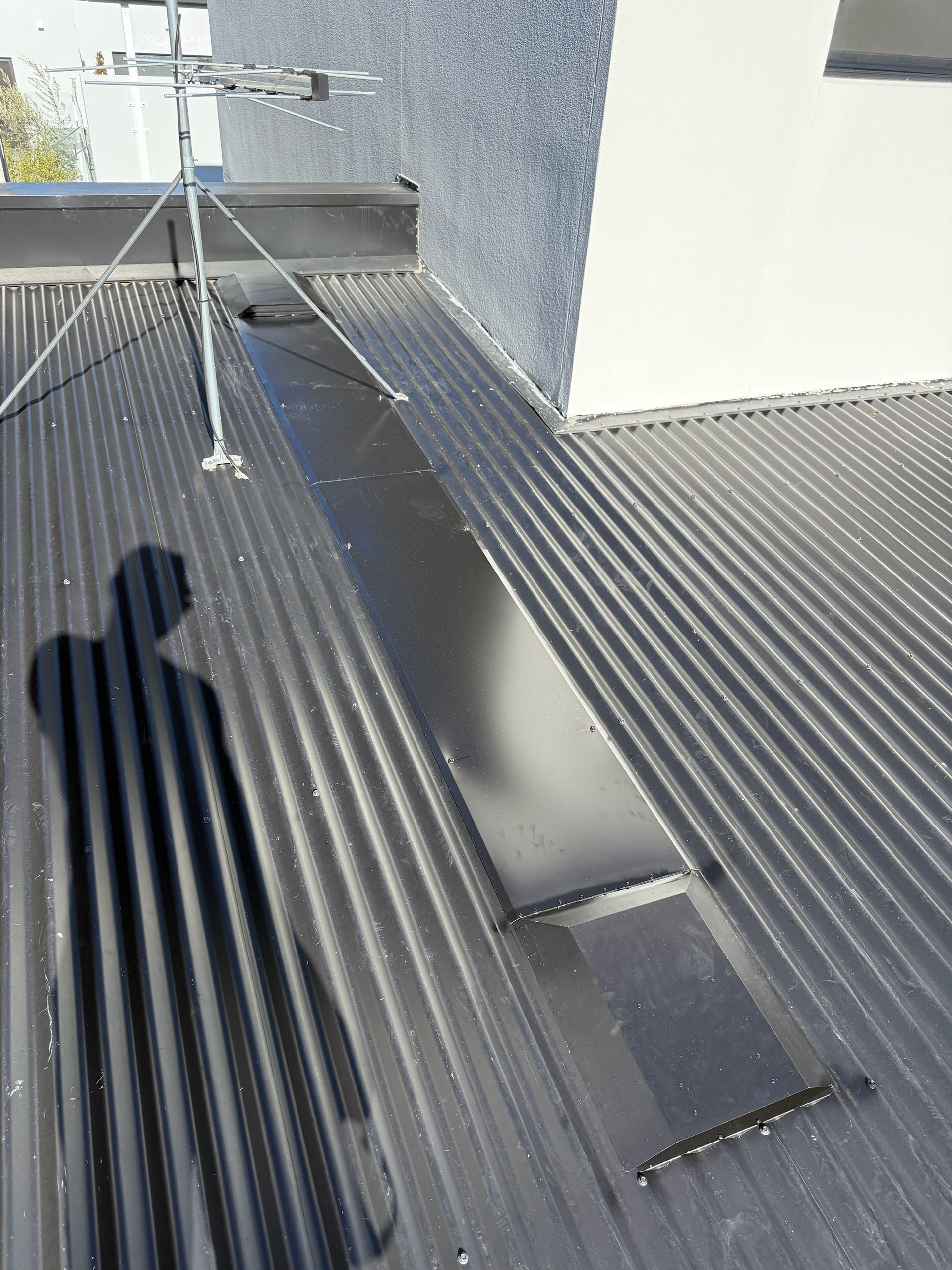 Black corrugated metal roof with a rectangular skylight and an antenna.— Vent Wise in Twin Waters, QLD