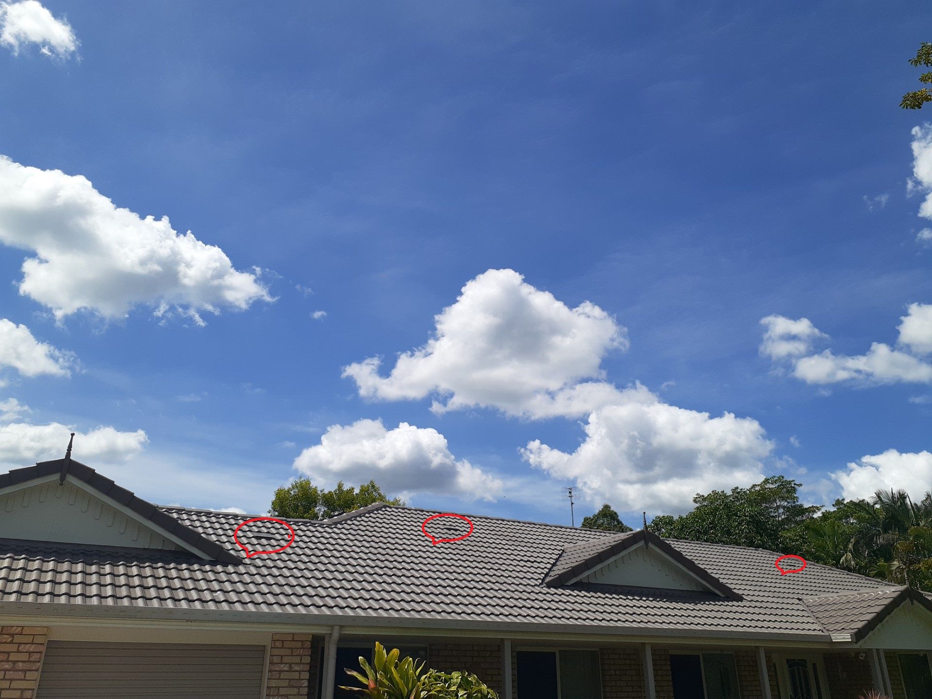 A gray tiled roof against a bright blue sky dotted with fluffy white clouds. Roof with red circles.— Vent Wise in Twin Waters, QLD