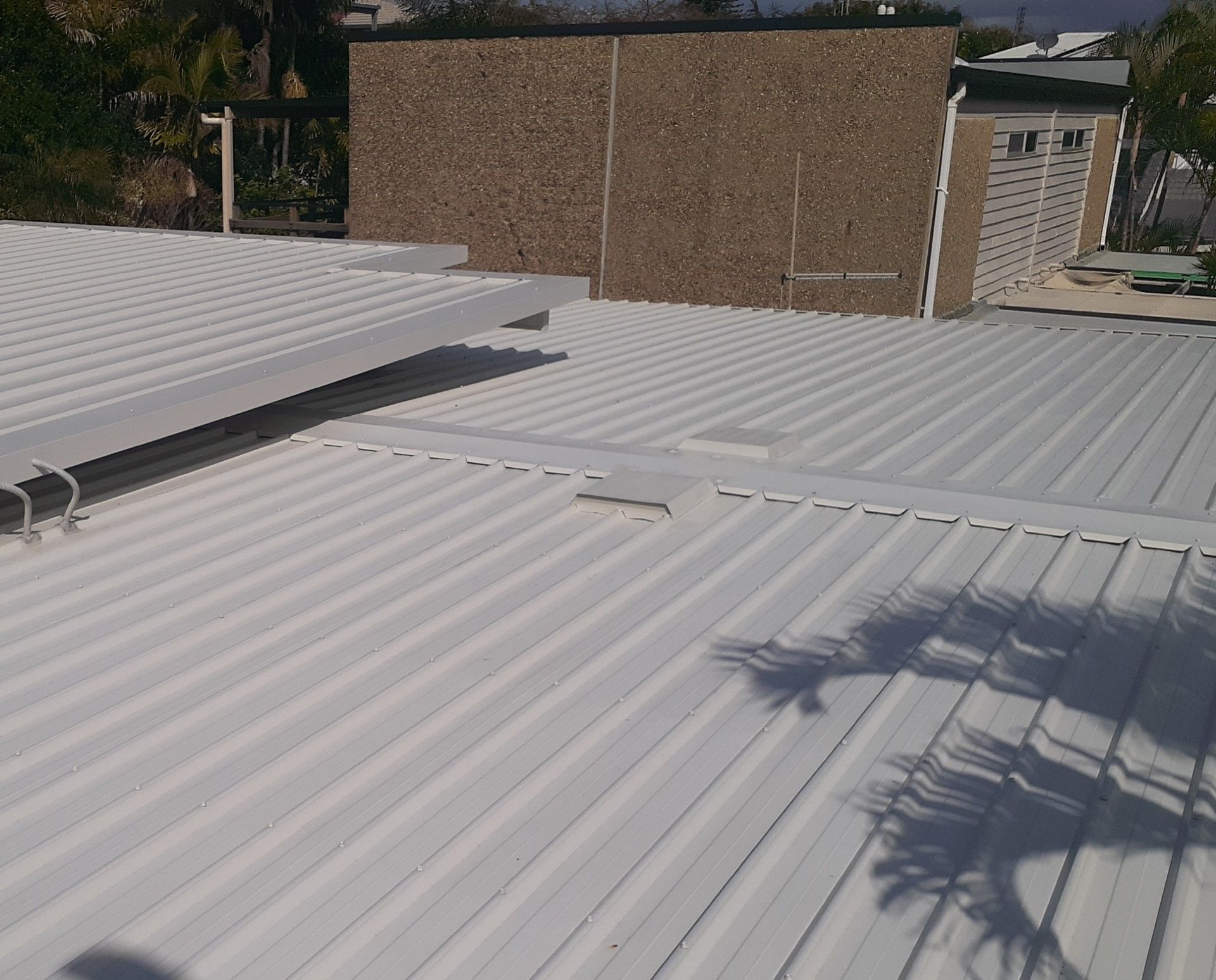 White corrugated metal roof with shadows cast on it, a brown brick wall in the background. — Vent Wise in Twin Waters, QLD
