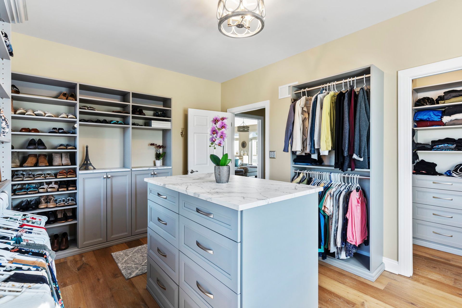 Walk-in closet with gray cabinets, island, clothing racks, and shelves for shoes.