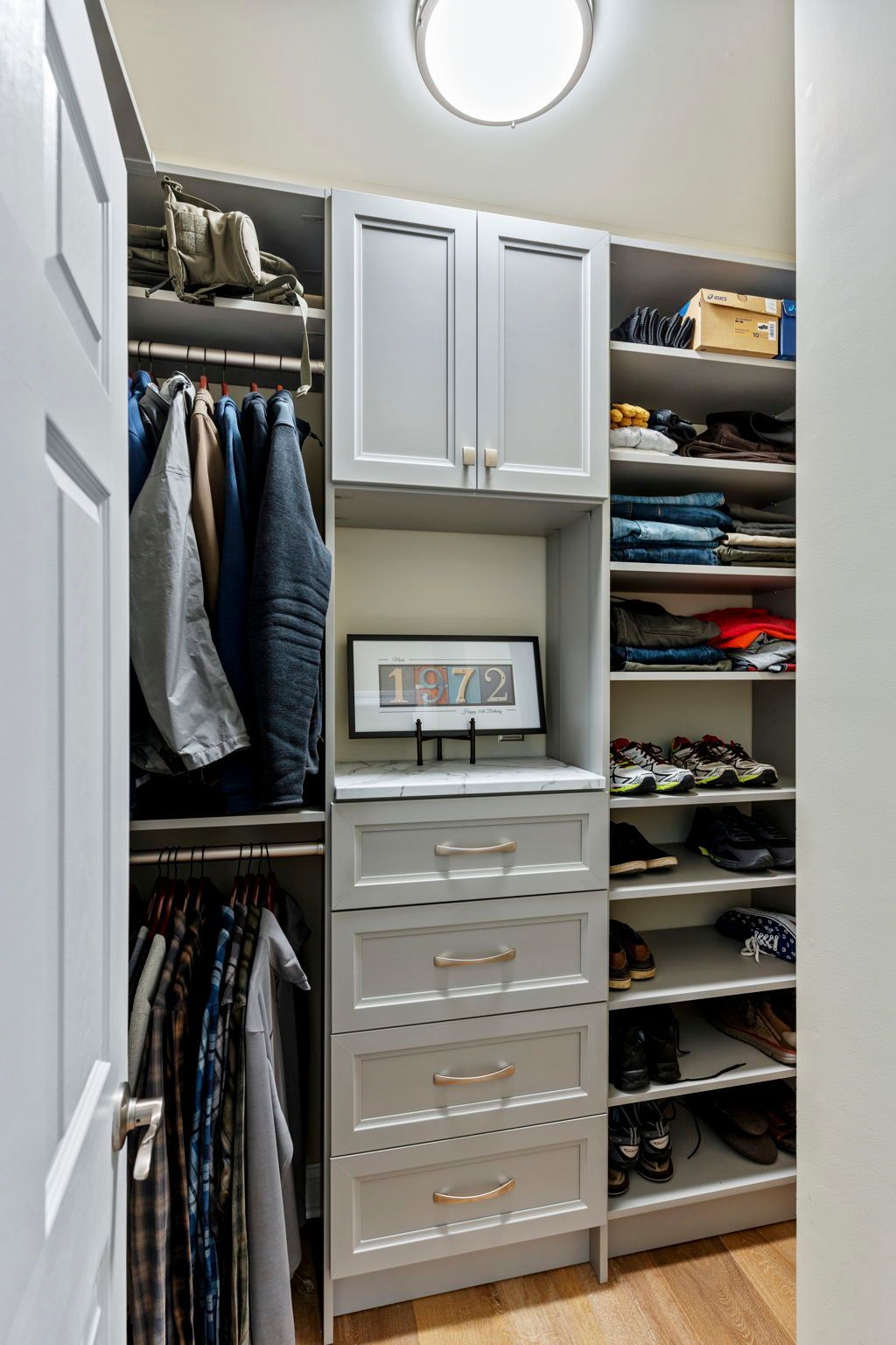 Closet with clothes on hangers, shelves with folded clothes & shoes, drawers, and cabinet, all light grey.