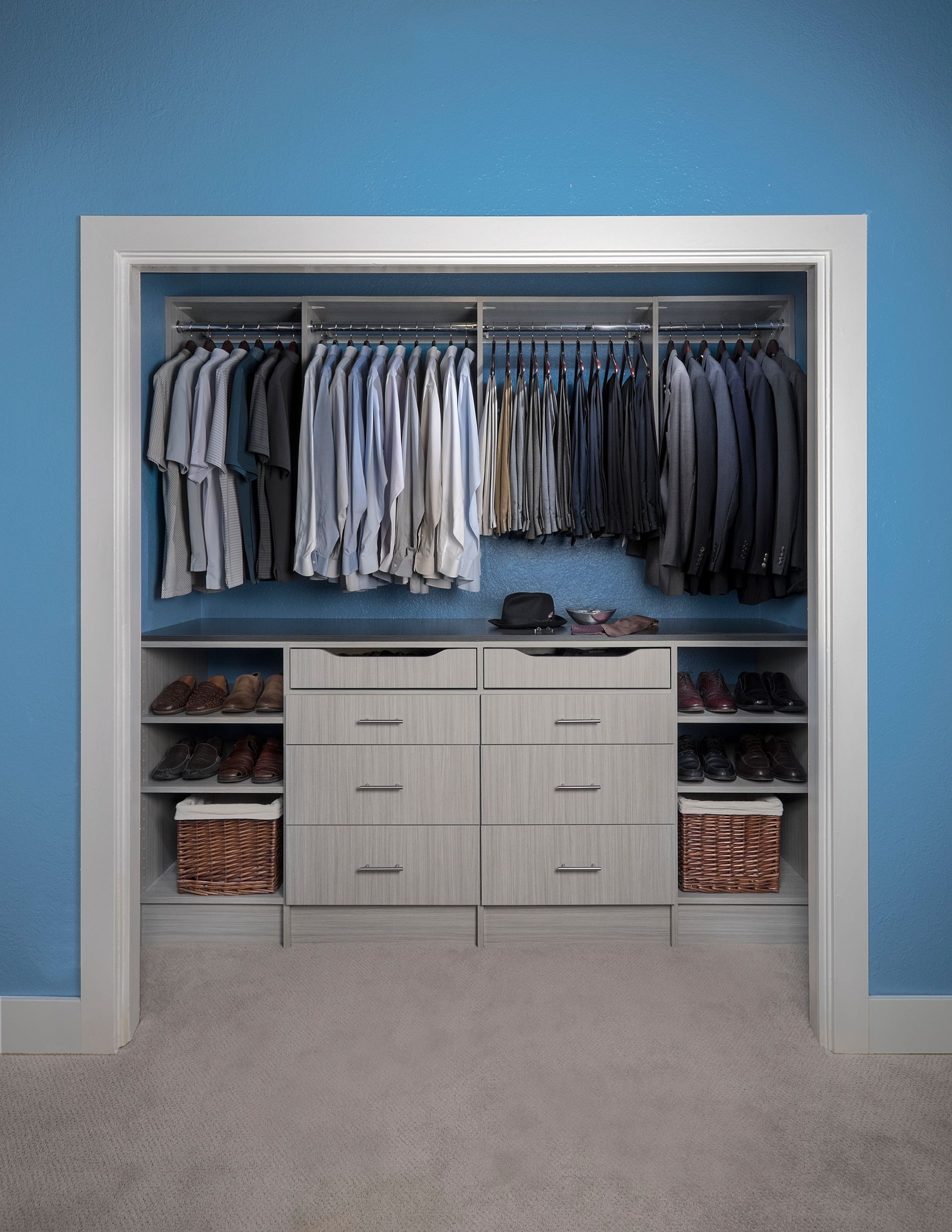 Walk-in closet with blue walls, white shelving, hanging clothes, and drawers in the center
