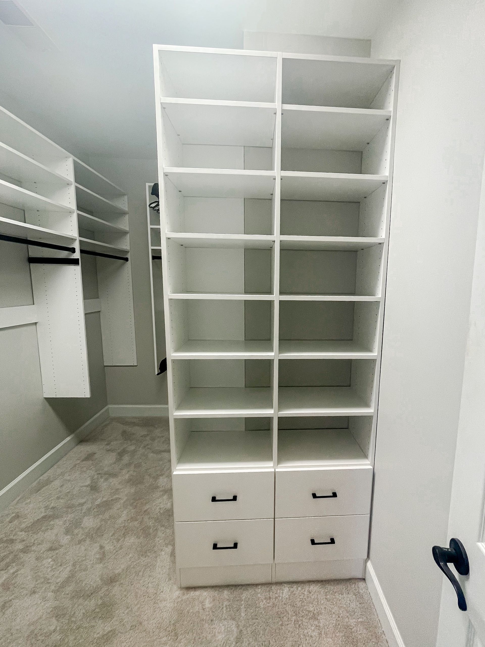 White closet shelving unit with drawers and open shelves in a room with carpet and a partially visible closet.