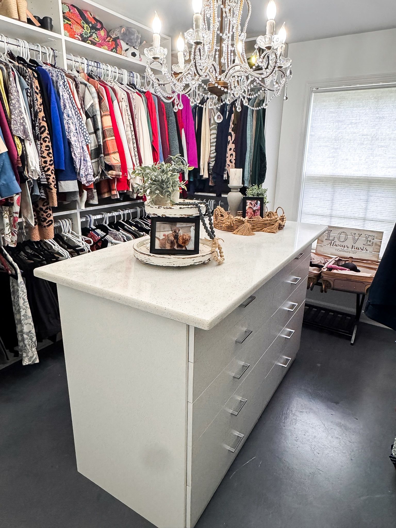 Walk-in closet with white island, clothes racks, chandelier, and a small chair.