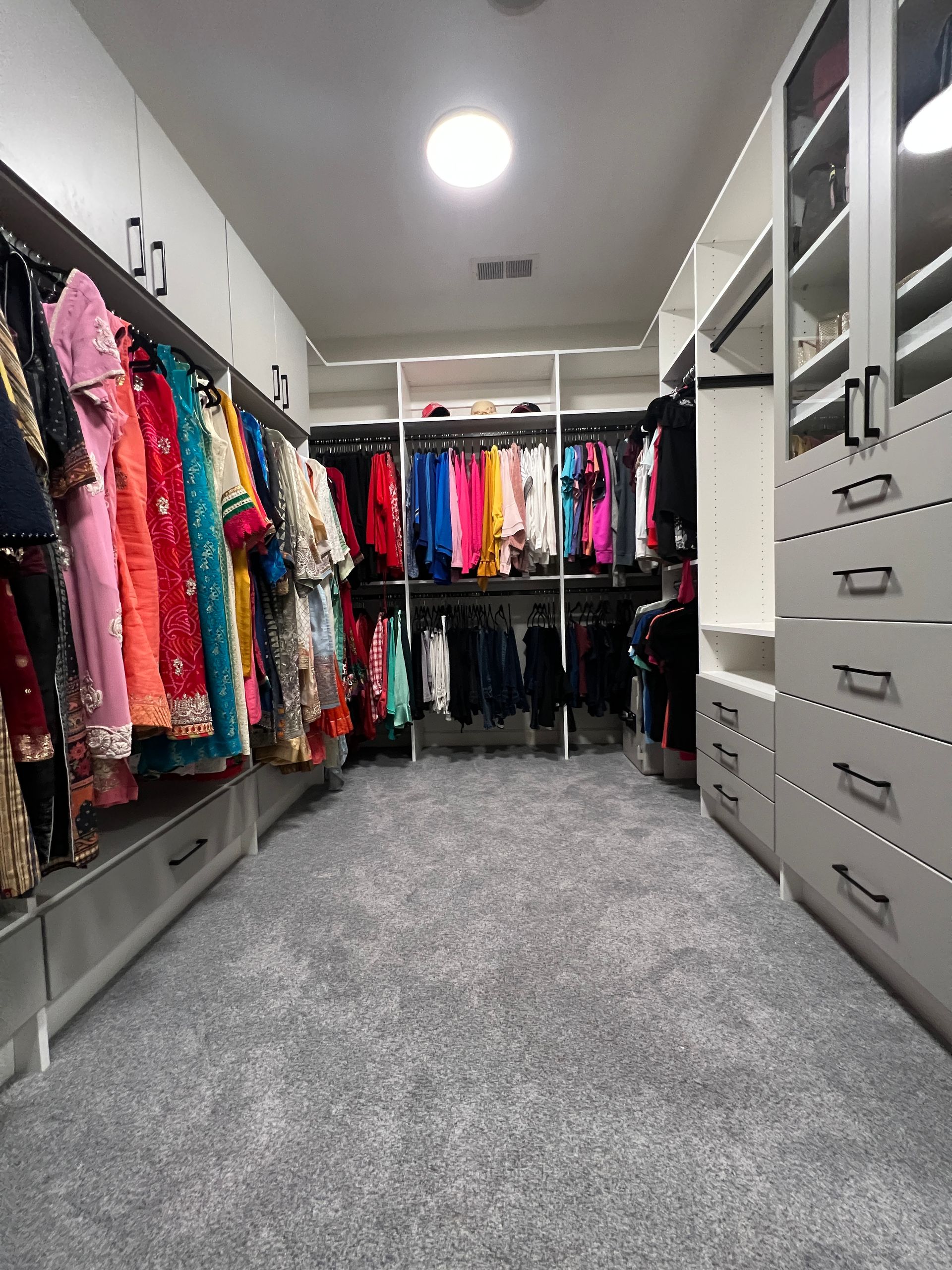Walk-in closet with colorful clothing racks and gray drawers. The floor is carpeted.