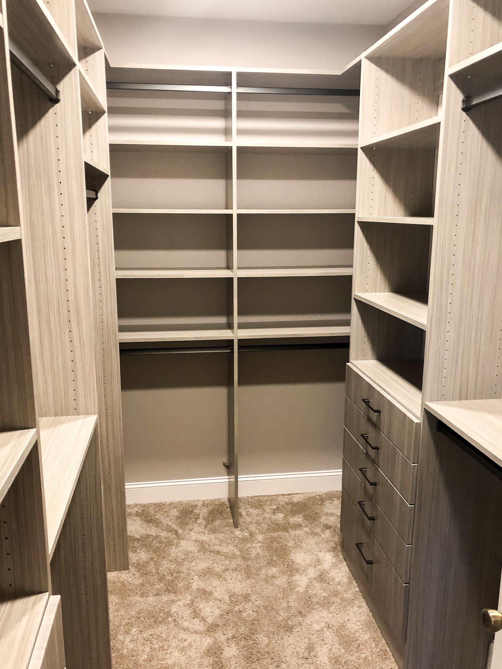 Walk-in closet with shelves and drawers in neutral tones, carpeted floor.