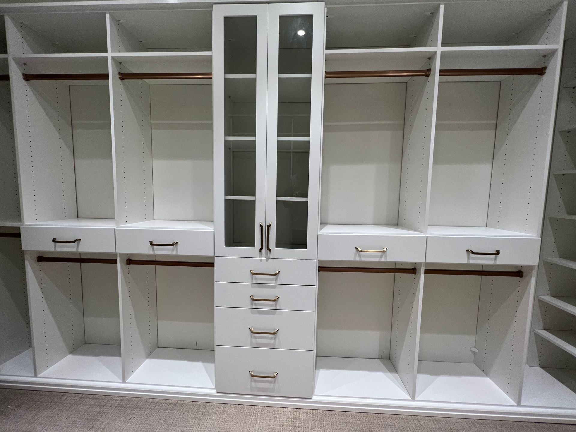 White, empty custom closet with rods, shelves, and drawers. Center cabinet has glass doors and drawers.