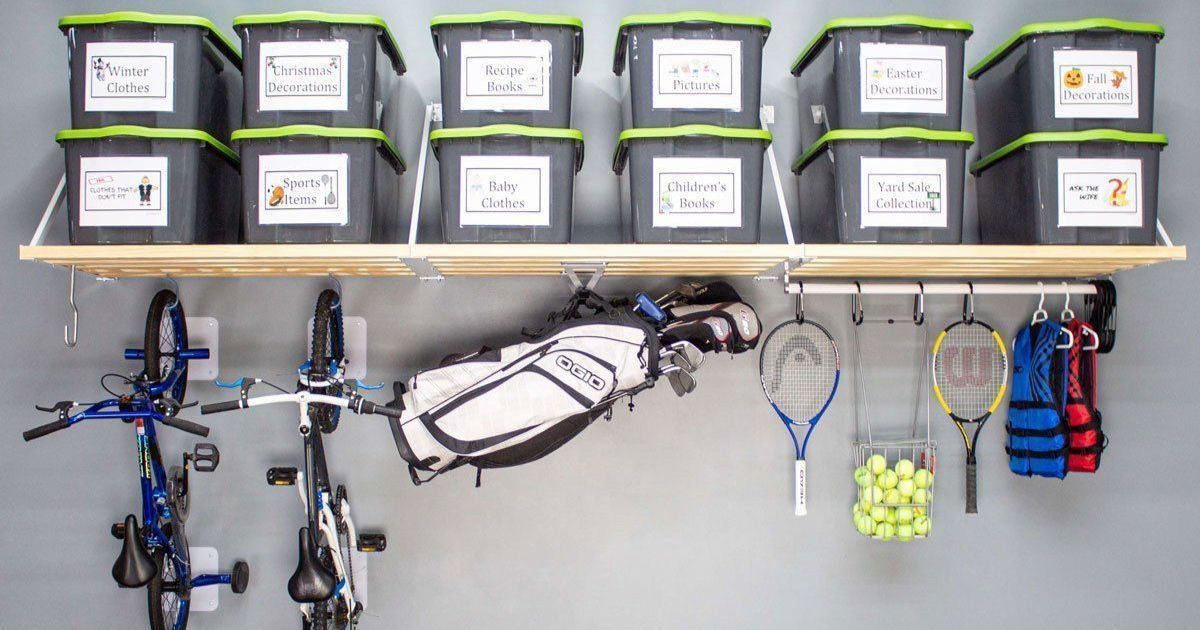 Wall-mounted bike storage with labeled gray bins, hanging bicycles, tennis rackets, balls, and sports gear