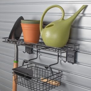 A green watering can sits on a shelf next to a shovel and pots