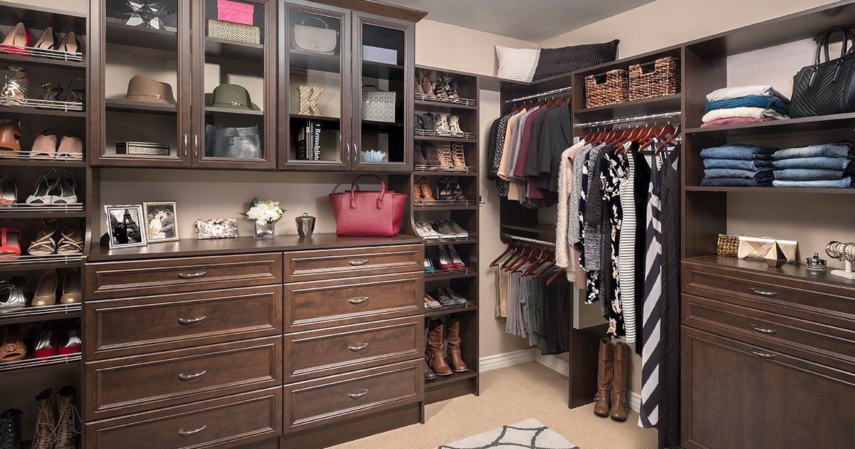 Walk-in closet with dark wood shelving displaying shoes, purses, and hanging clothes.