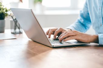 Person typing on a laptop at a wooden desk in a bright office