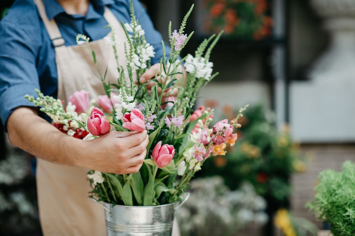 Florist arranging pink and white flowers in a metal bucket at an outdoor market