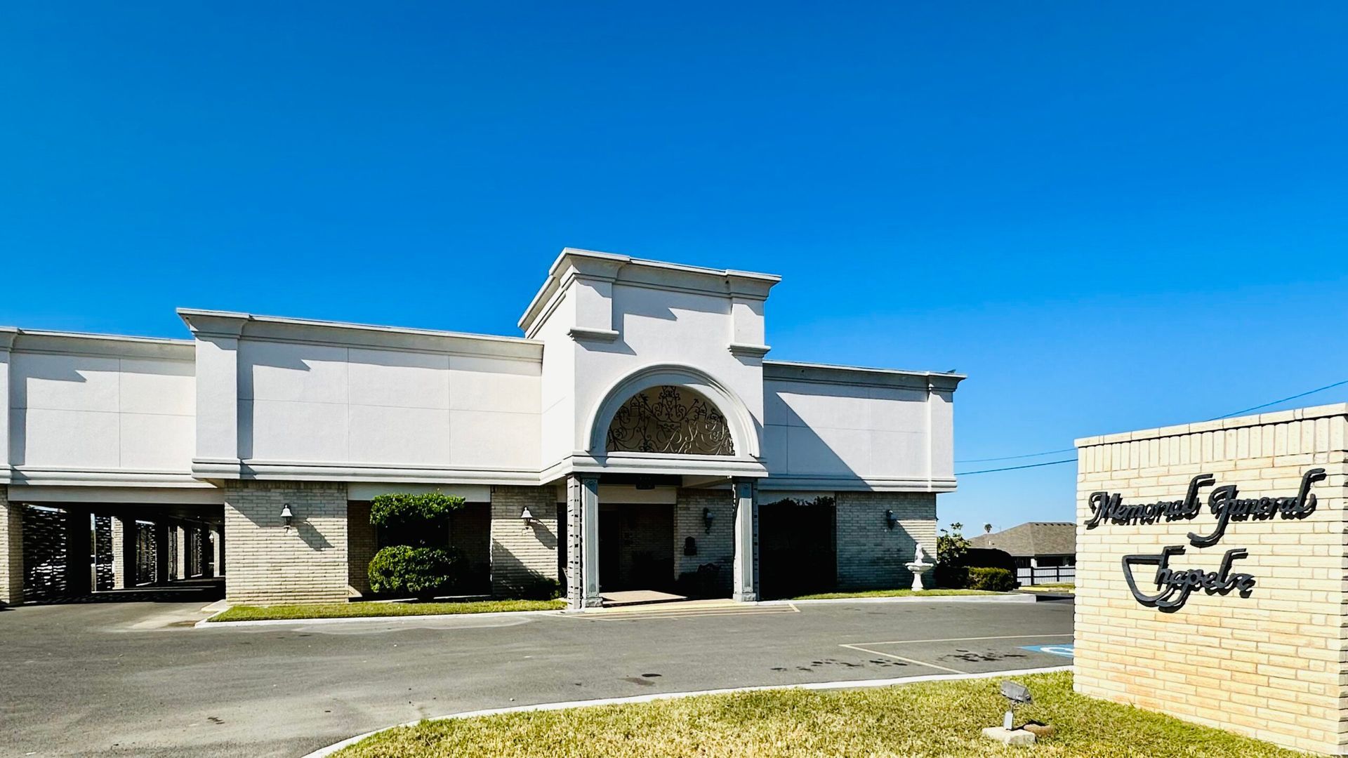 Low white building with arched entrance and sign beside it under a clear blue sky
