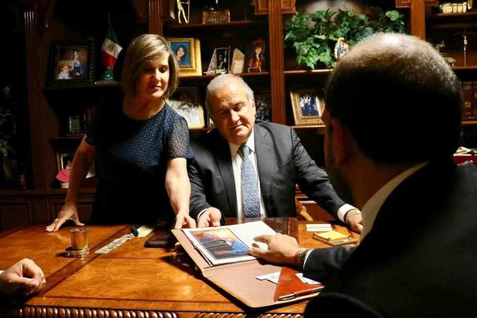 Three people in a wood-paneled office reviewing documents across a wooden table