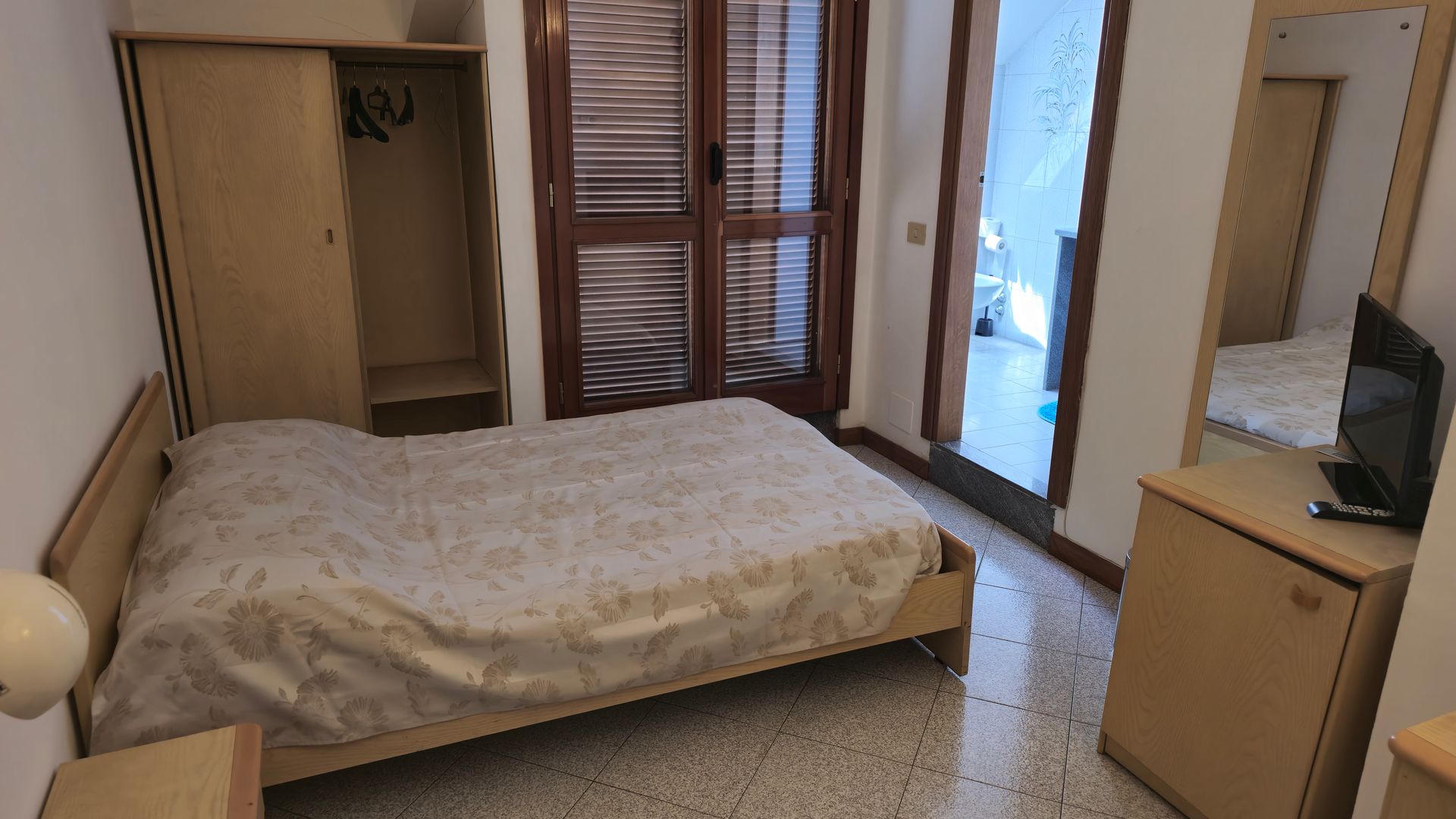 Una camera da letto con letto, comodino, specchio e televisione.
