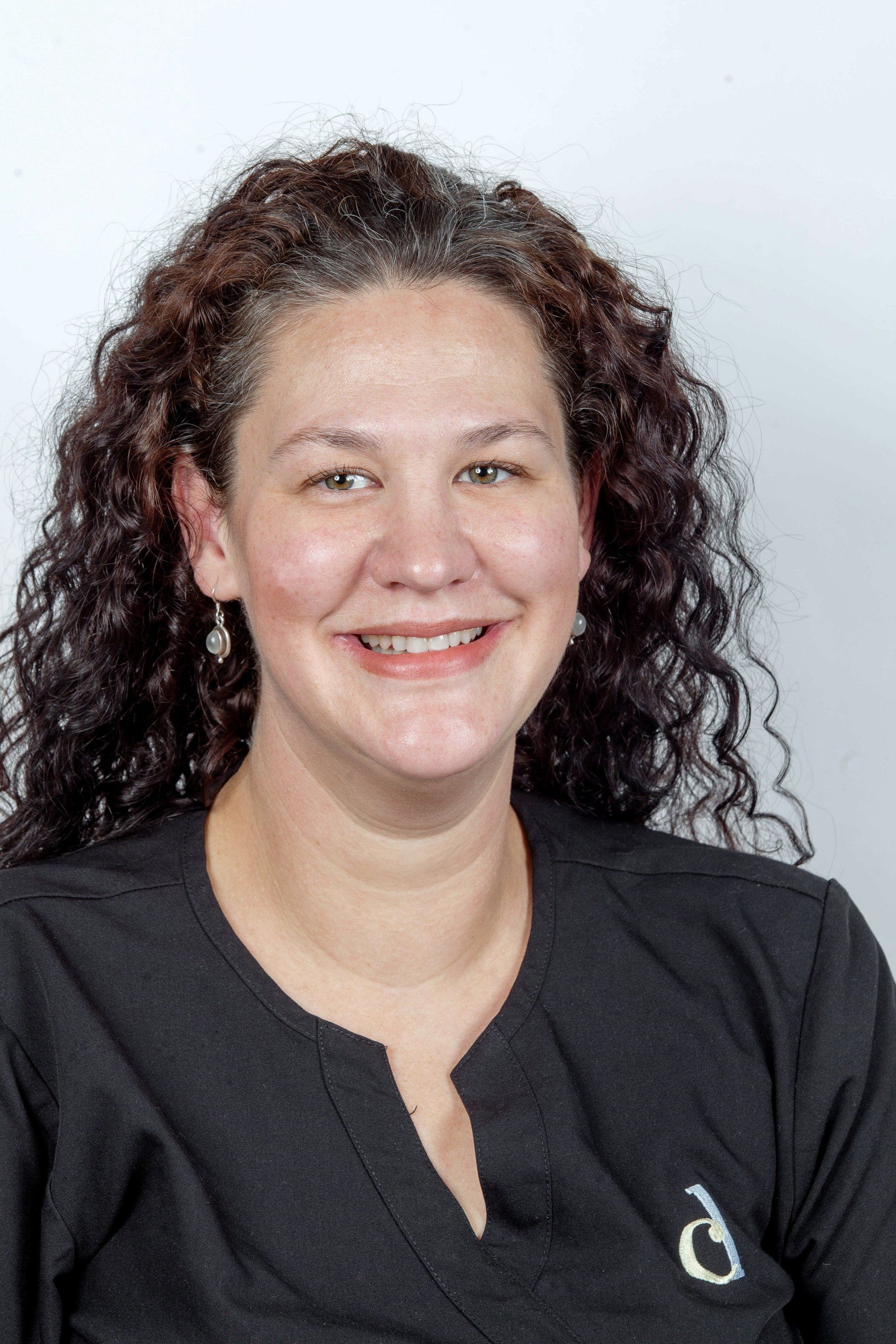 Portrait of a smiling person with curly hair in a black top against a light background
