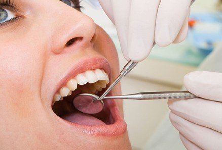 Dentist examining a patient’s open mouth with dental tools and gloves