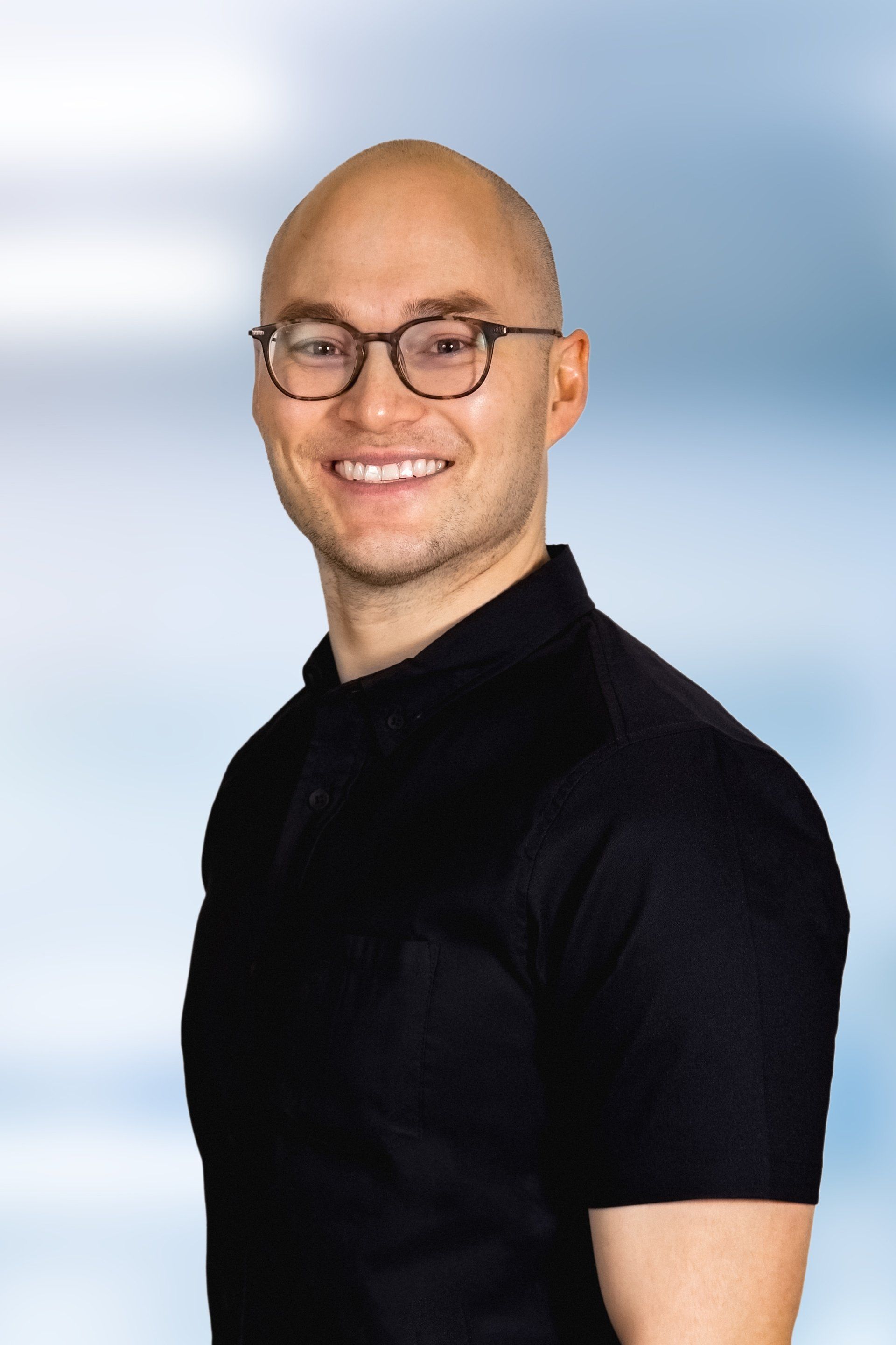 Portrait of a smiling bald man in glasses wearing a black shirt against a soft blue background