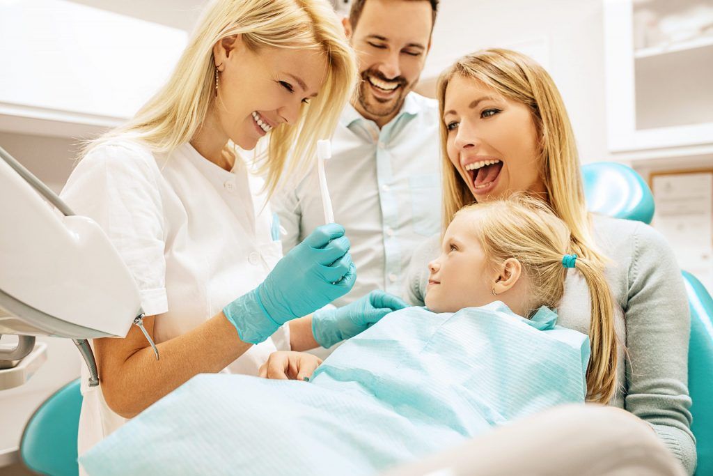 Dentist and family smiling during a child’s dental exam in a bright clinic