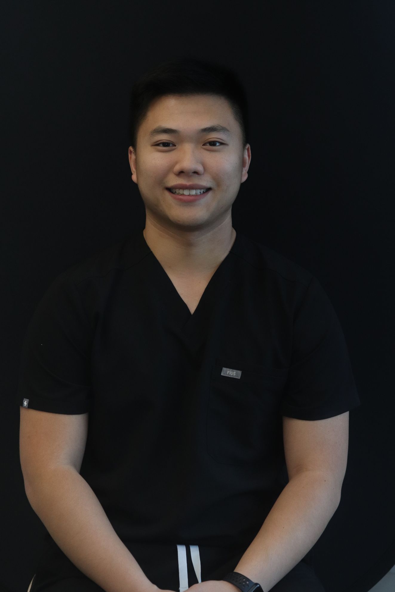 Smiling person in black shirt seated against a dark background