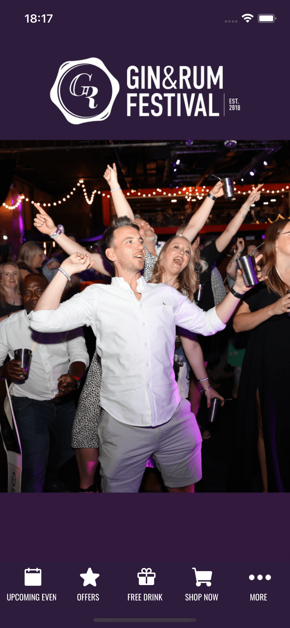 People dancing at a gin & rum festival. Man and woman in the center with arms up. Purple background.