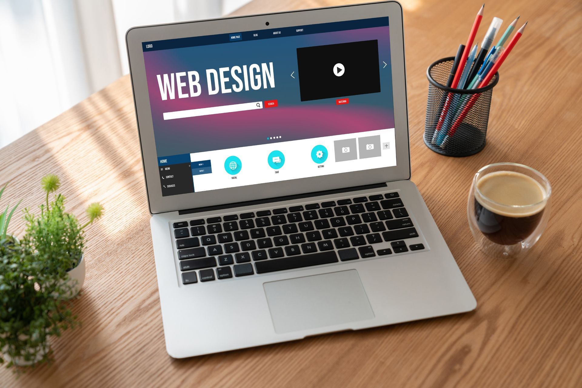 Laptop displaying a web design interface, next to art supplies and coffee.