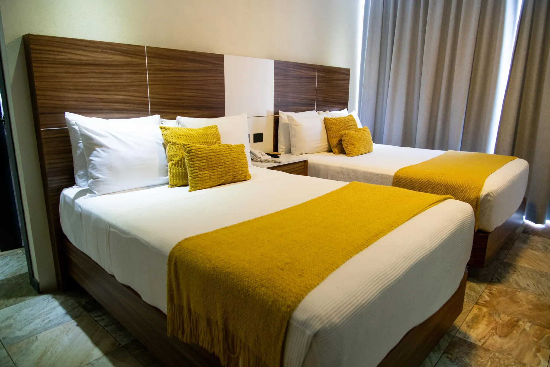 Dos camas individuales bien hechas con mantas y almohadas amarillas en una luminosa habitación de hotel.