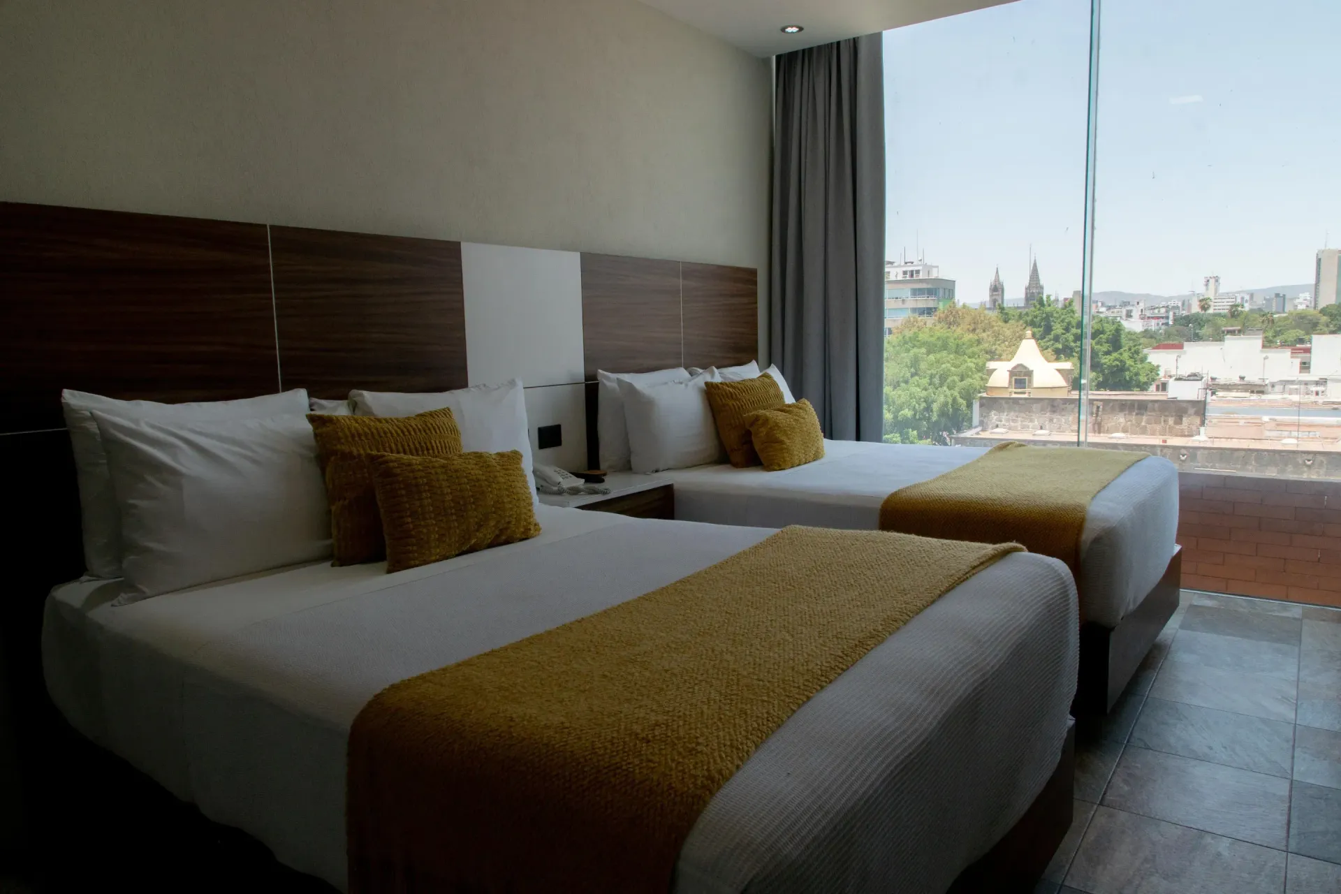 Habitación de hotel moderna con dos camas y vistas a la ciudad a través de una gran ventana.